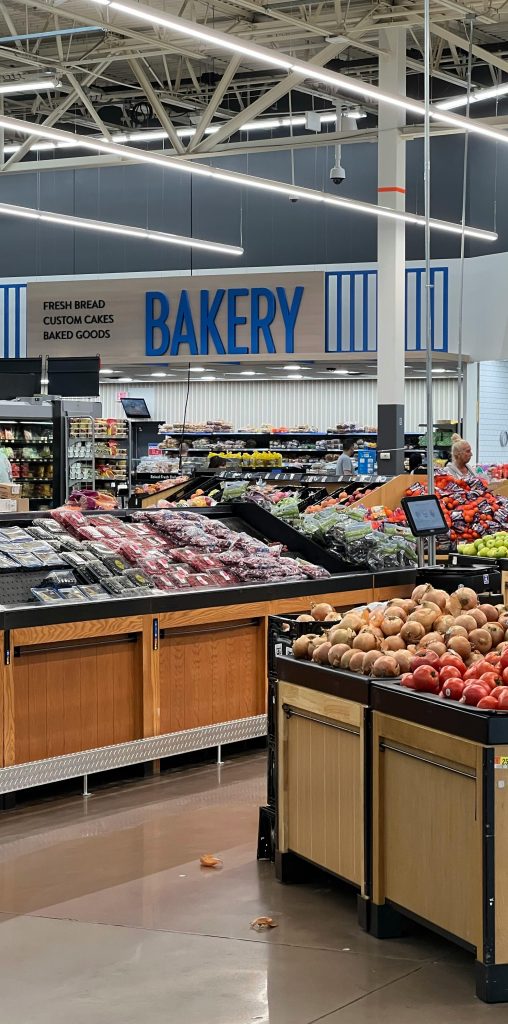 Modern grocery store produce section with fresh fruits and bakery signs.